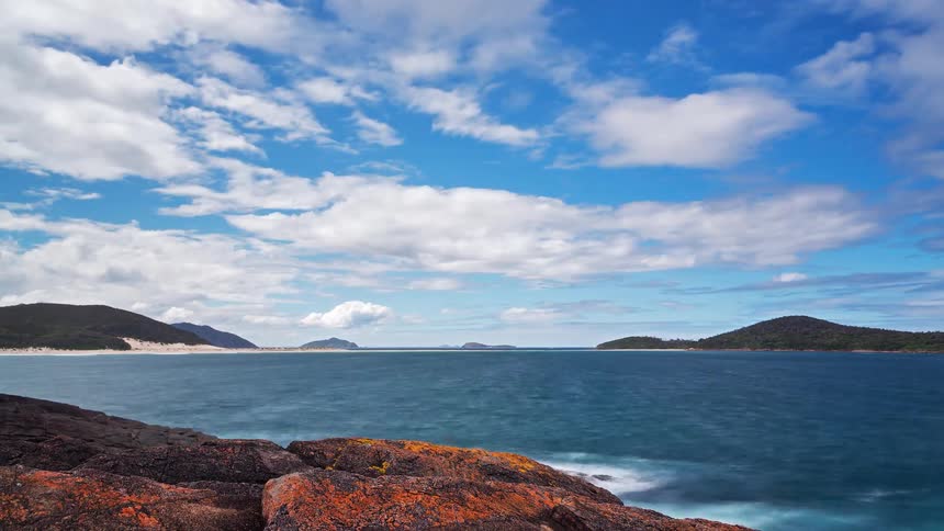 A beautiful time-lapse of a pristine ocean bay with fast-moving clouds and smooth waves seen from a rocky shoreline