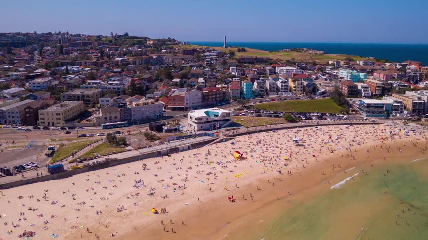 A sweeping aerial shot pulls back to reveal the iconic and crowded Bondi Beach in Sydney, Australia on a bright sunny day
