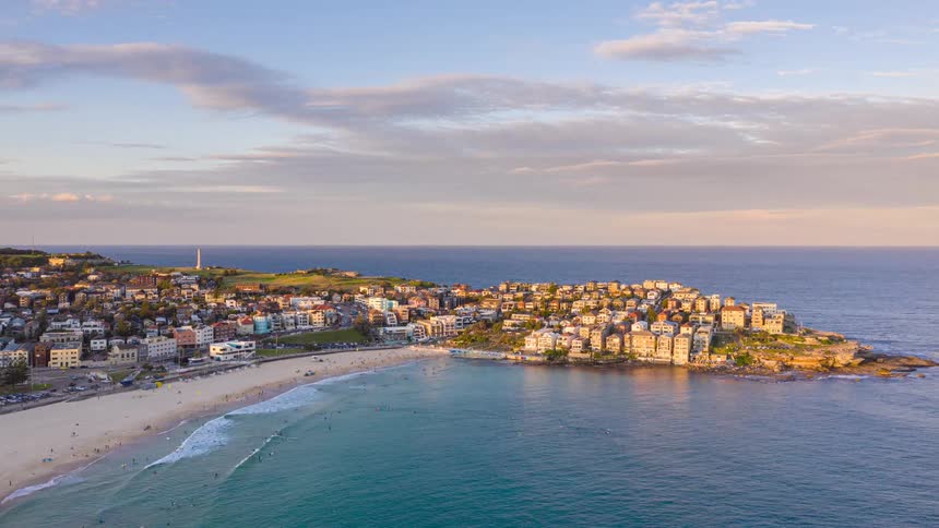 An expansive aerial hyperlapse view of Sydney's iconic Bondi Beach during a beautiful golden hour sunset