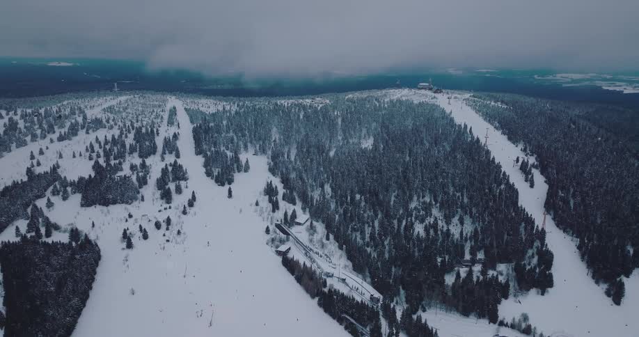 An expansive aerial view captures the ski slopes and lifts of a winter resort covering a forested mountain under a cloudy sky