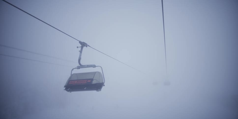 An empty chairlift slowly emerges from the thick, white fog and passes by on a cold and eerie winter day