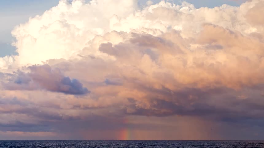 A dramatic timelapse of golden hour clouds and a rainbow forming over the ocean
