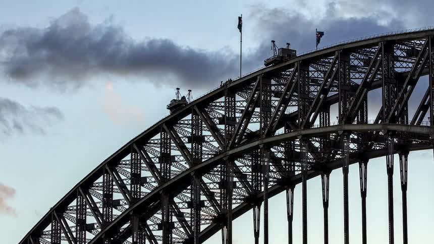 A dramatic time-lapse of clouds passing over the arch of the Sydney Harbour Bridge as the Australian flag waves at sunset