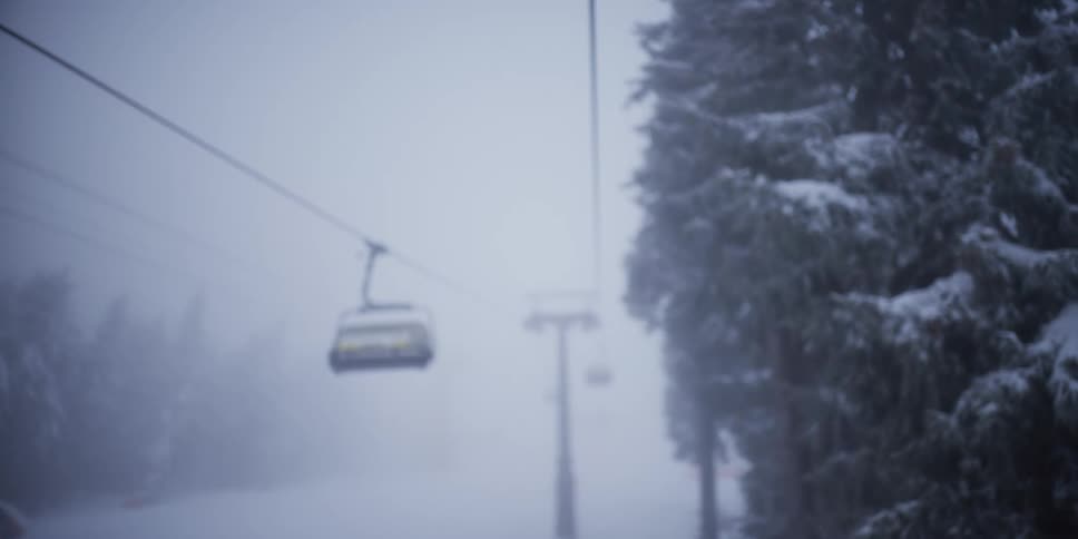 A blurry, atmospheric shot of an empty ski lift moving through a foggy snowstorm
