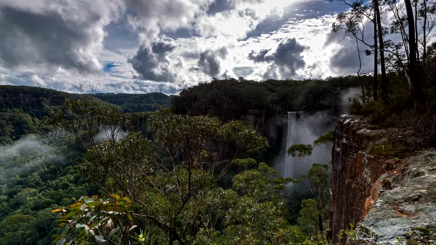 A majestic timelapse reveals a stunning waterfall as mist and clouds roll through a lush, forested valley