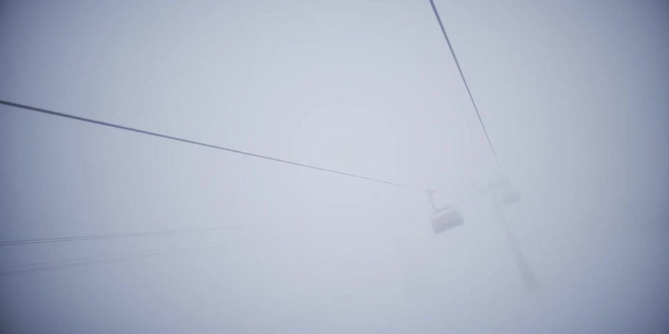 An empty ski lift chair slowly emerges from and disappears into the dense, white fog at a desolate ski resort