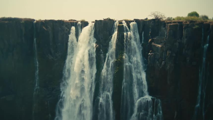 A wide shot shows a powerful waterfall cascading over a sheer rock cliff