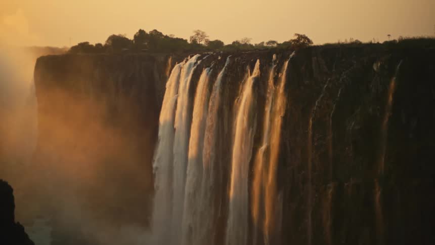 Stunning view of a massive waterfall cascading over a cliff, illuminated by the warm glow of sunset