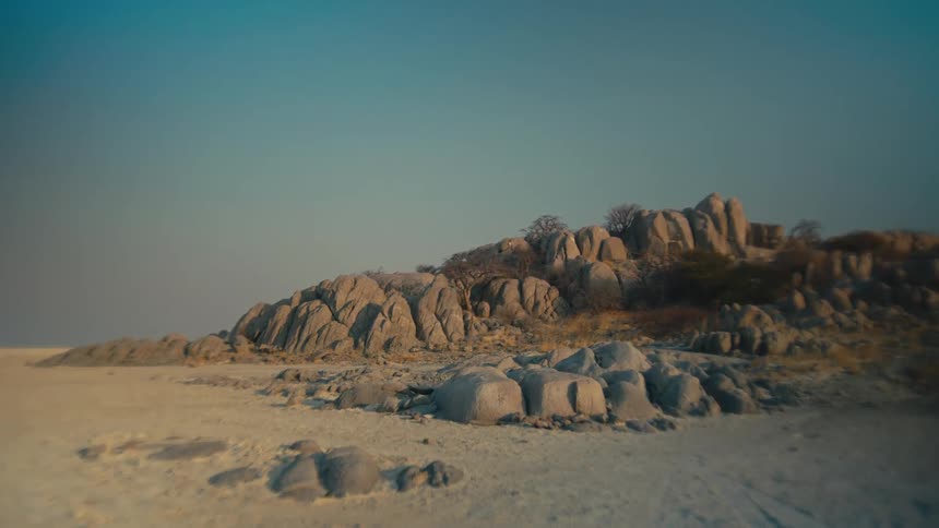 A serene timelapse shows the morning sun casting long shadows over a rocky island in a vast, arid salt pan