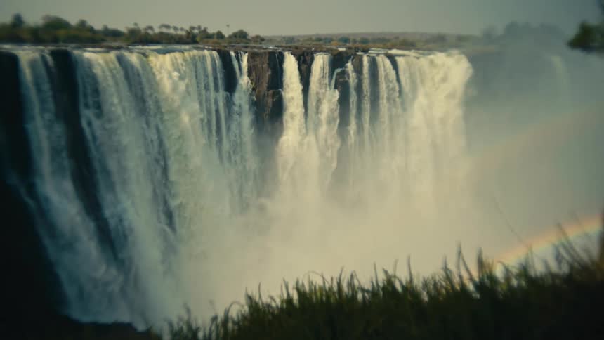 A slow zoom out reveals the immense scale of Victoria Falls, with a beautiful rainbow forming in the misty spray