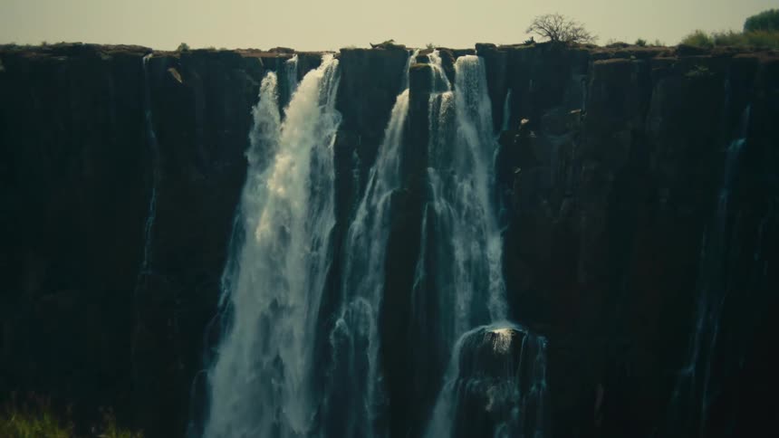 A dramatic tilt up shot reveals the majestic Victoria Falls cascading down a massive rock cliff