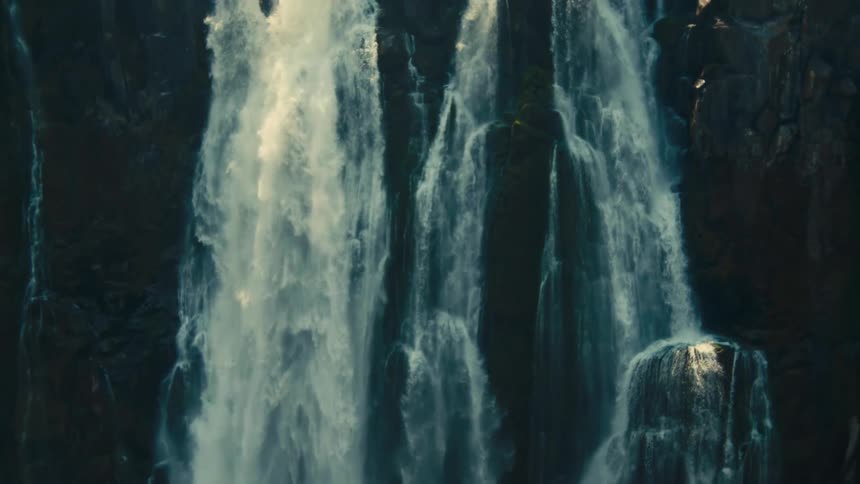 A majestic waterfall cascades down a dark, rugged cliff face in a dramatic slow-motion close-up