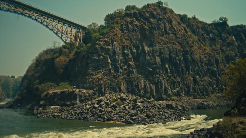 The iconic Victoria Falls Bridge spans a deep, rocky gorge as the powerful Zambezi River rushes below