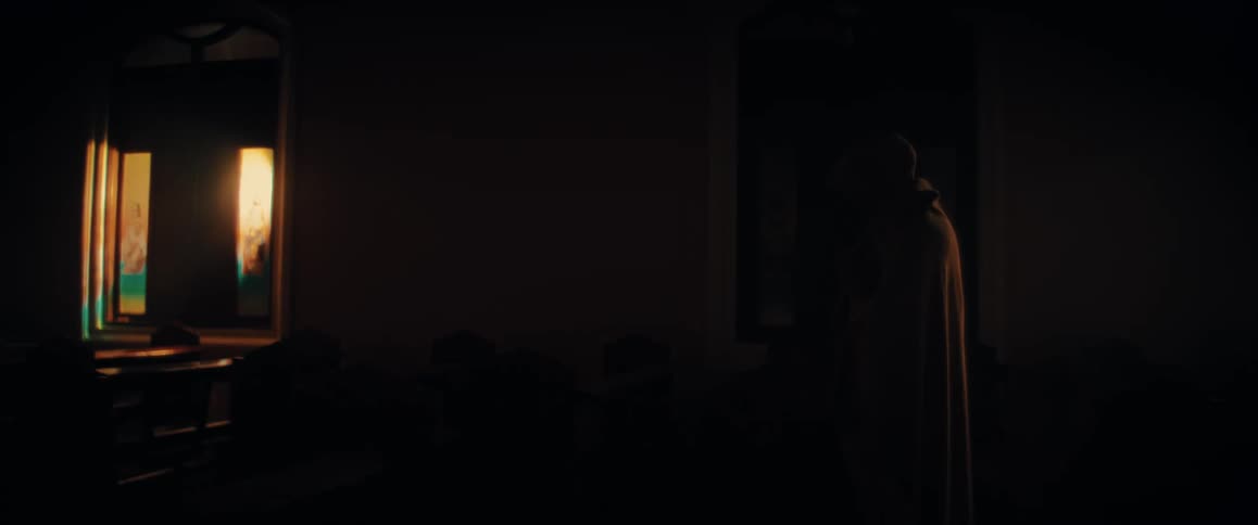 A mysterious hooded figure prays in silhouette, bathed in a dramatic ray of light streaming through a window in a dark, empty church