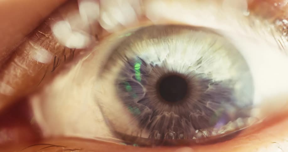 A macro shot of a human eye as the pupil dilates and the light fades from bright to dark, revealing futuristic reflections