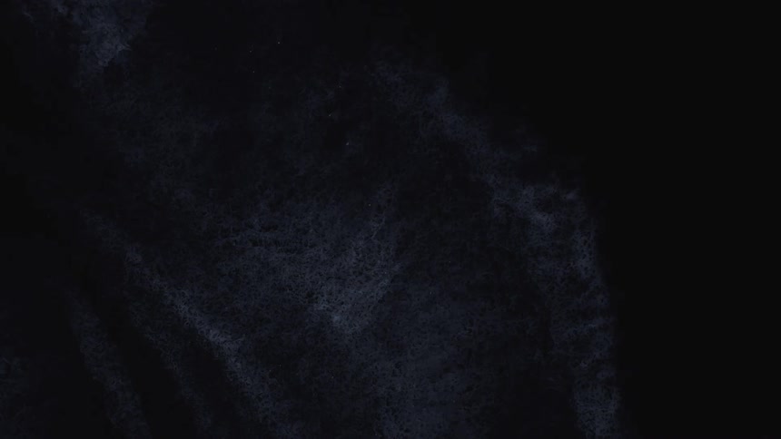 A dark, textured, grey-blue substance with a web-like pattern slowly dries and fades into a black background