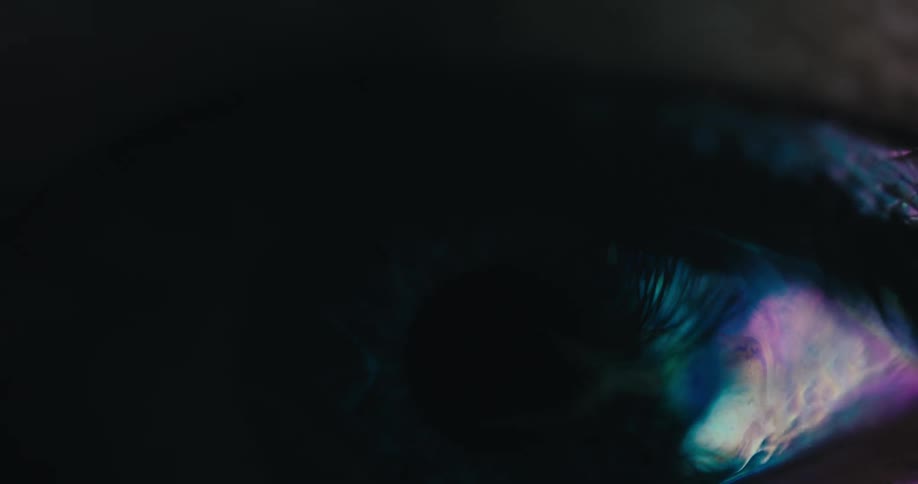 In a dramatic slow-motion macro shot, colorful light reveals the intricate details of a vibrant blue human eye as its pupil constricts