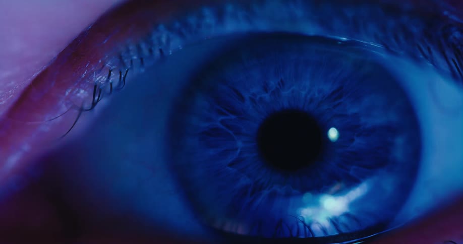 A mysterious close-up reveals a striking blue human eye, with the iris and pupil coming into sharp focus under a dark blue light