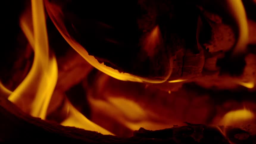 A mesmerizing close-up of a roaring fire with bright flames licking at glowing embers in a fireplace