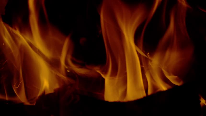 Close-up slow-motion shot of warm, vibrant flames dancing over glowing embers against a dark background
