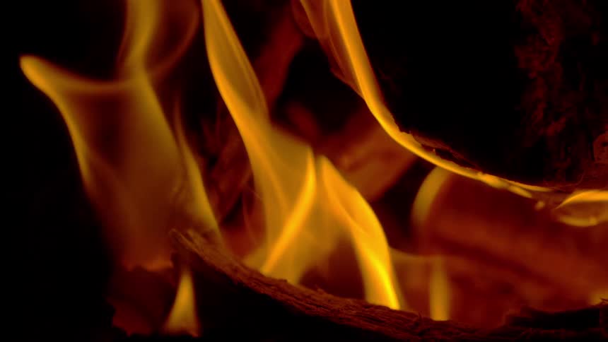 Golden flames dance in mesmerizing slow motion over burning logs against a dark background