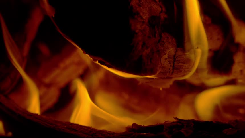 Vibrant yellow flames dance in slow motion over burning logs in a cozy fireplace