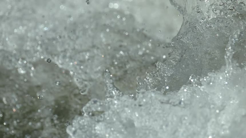 An extreme close up in super slow motion shows turbulent water splashing, bubbling, and glistening in the sun