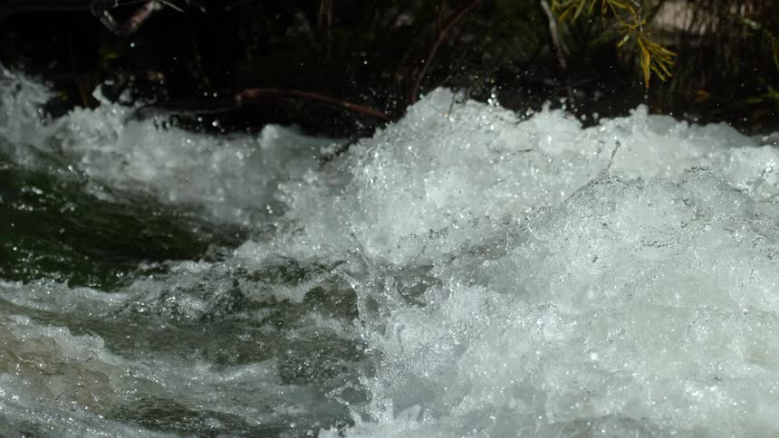 A close-up, super slow-motion shot of a turbulent river as whitewater churns and splashes