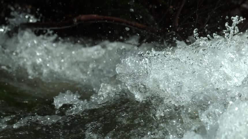 A super slow-motion close-up captures the powerful, churning white water of a fast-moving stream