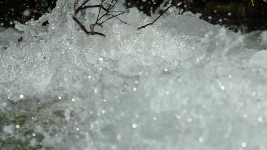 A powerful stream of water crashes and churns in a turbulent river in an extreme close-up slow-motion shot
