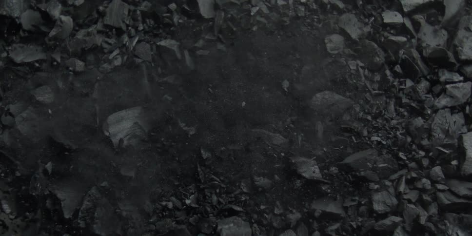 A top-down view of fine black dust blowing across a bed of charcoal in slow motion