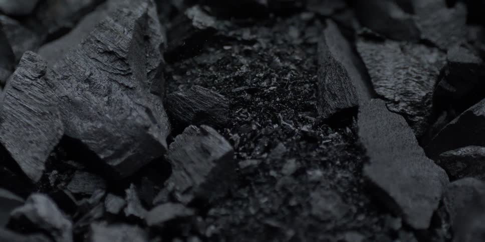 Slow motion macro shot of black charcoal pieces and dust vibrating and shifting