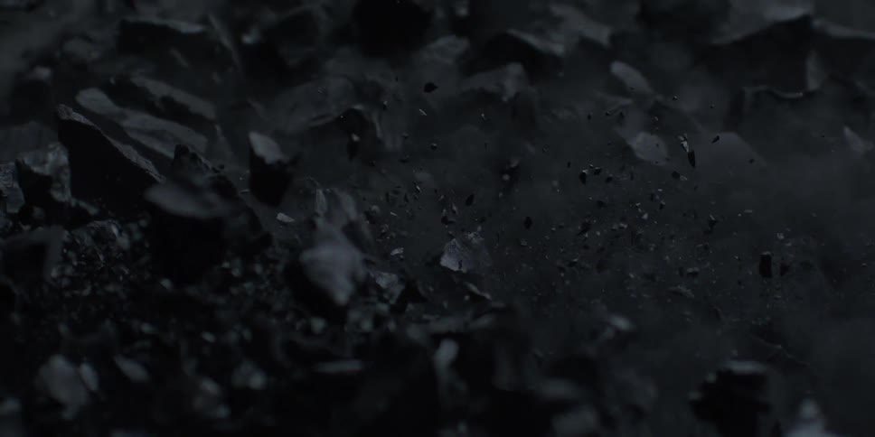 A dramatic close-up in slow motion shows dark, rocky material exploding into dust and debris