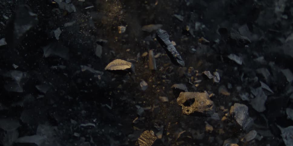A pile of charcoal explodes upwards in a dramatic, top-down, slow-motion shot