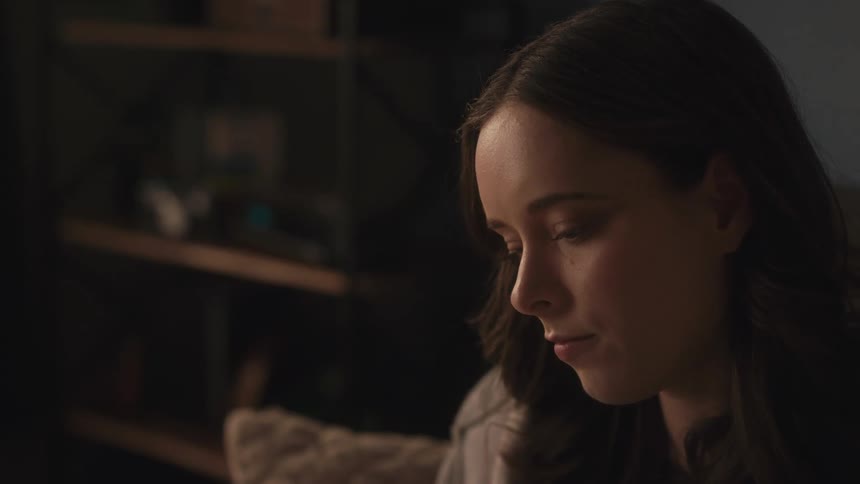 A close-up shot of an introspective young woman with a pensive expression in a dimly lit room