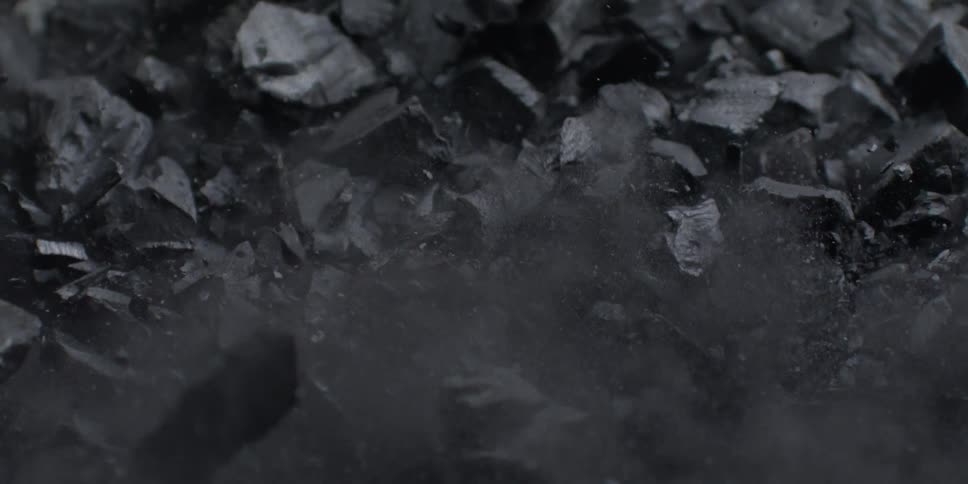 A pile of black charcoal erupts in a dramatic, super slow-motion explosion of dust and fragments