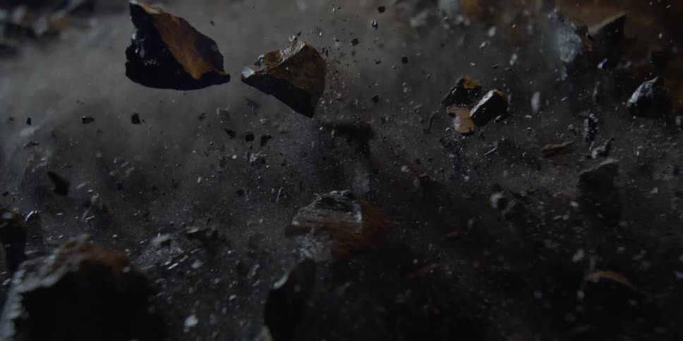 An explosion sends shards of black rock and dust flying upwards in super slow motion