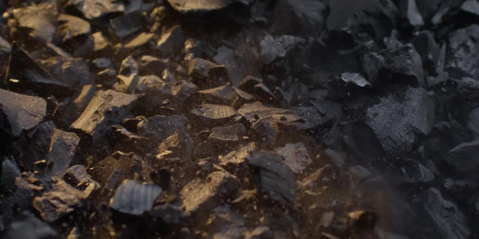 Warm light illuminates pieces of black charcoal as they violently shake and create dust in slow motion