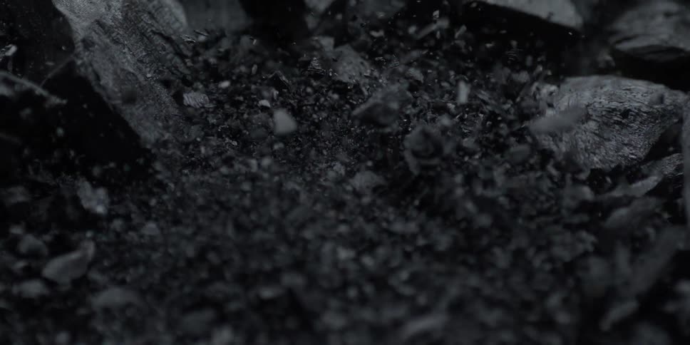 A dramatic super slow motion macro shot of black charcoal dust and fragments exploding upwards