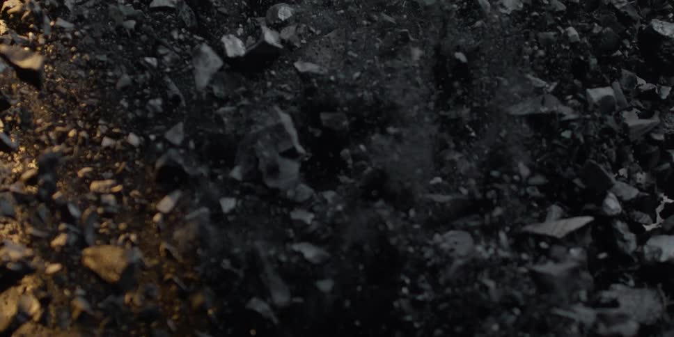 A pile of black charcoal explodes upward in a dramatic cloud of dust and debris in slow motion