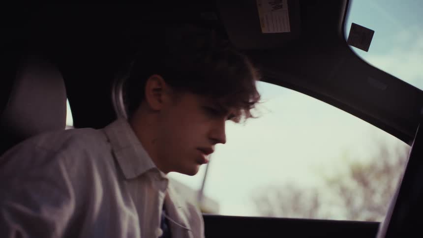 An upset young man gets into his car, has an emotional moment, and then anxiously checks his phone