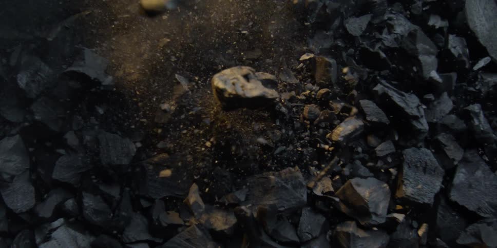 An overhead slow motion shot captures a piece of charcoal exploding on impact, sending fragments and dust into the air
