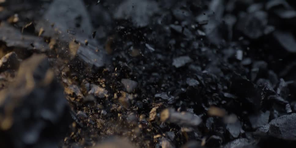 Super slow motion of exploding charcoal pieces shattering against a dark background