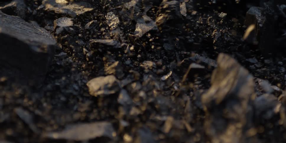 A super slow-motion macro shot captures dust and ash particles swirling over pieces of charcoal