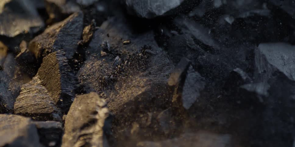 Black charcoal briquettes explode upwards in a dramatic super slow motion macro shot