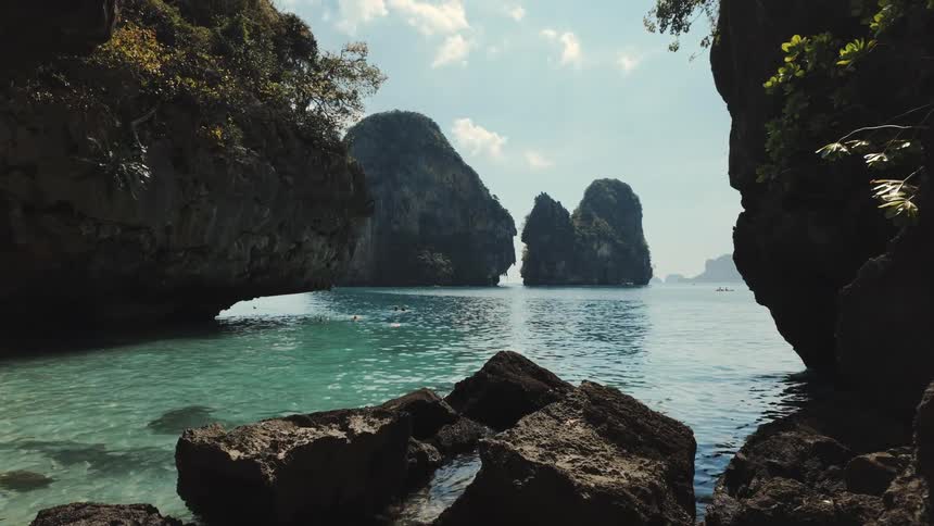 A picturesque tropical bay framed by rock formations, revealing turquoise waters and majestic limestone karsts under a sunny sky