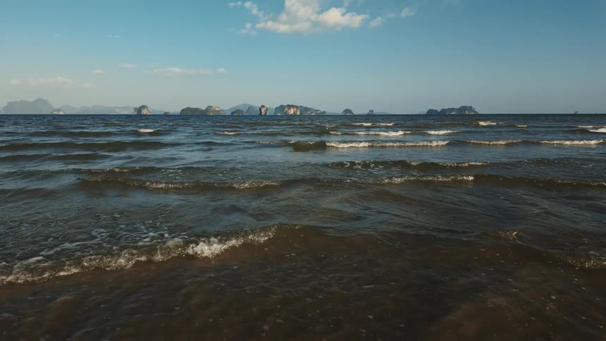 A scenic tilt-up reveals a vast ocean with gentle waves lapping the shore and a stunning vista of tropical islands on the horizon