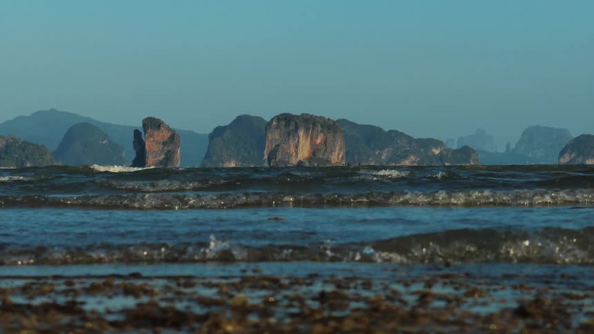 Slow motion waves gently lap a rocky shore with a stunning backdrop of tropical limestone islands