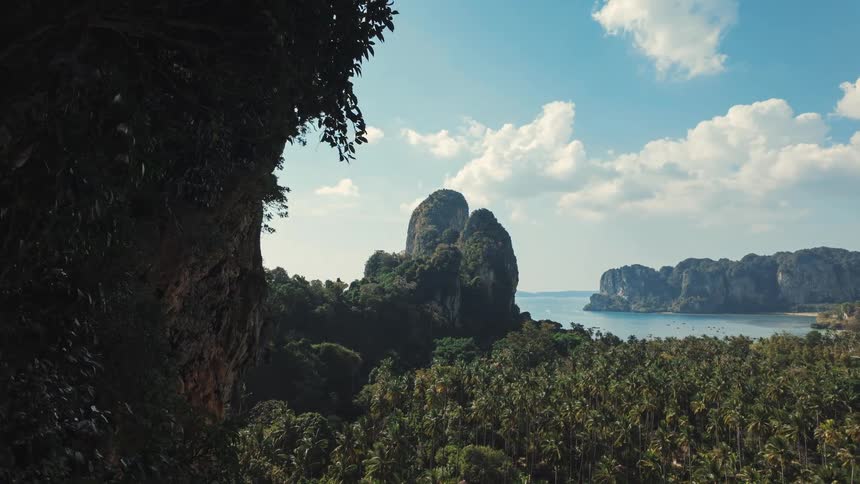 A breathtaking clifftop view reveals a lush tropical valley filled with palm trees, majestic limestone karsts, and a serene bay