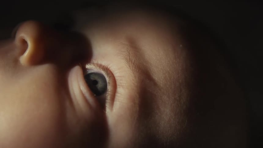 An extreme close-up shot of a newborn baby's eye looking up with curiosity in a dimly lit room